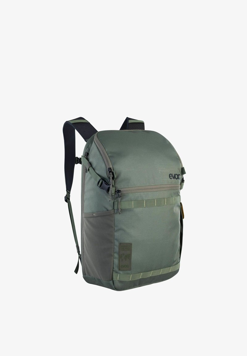 Zaino in tessuto verde con parte superiore arrotondata, scomparto frontale con cerniera, cinturini decorativi e tasca in rete. Comprende un logo e un pannello laterale con trama.