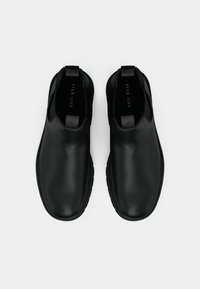 Zapatos negros sin cordones con acabado de cuero suave, diseño de punta redondeada, detalles de costura sutiles y una pestaña en el talón para facilitar el uso.