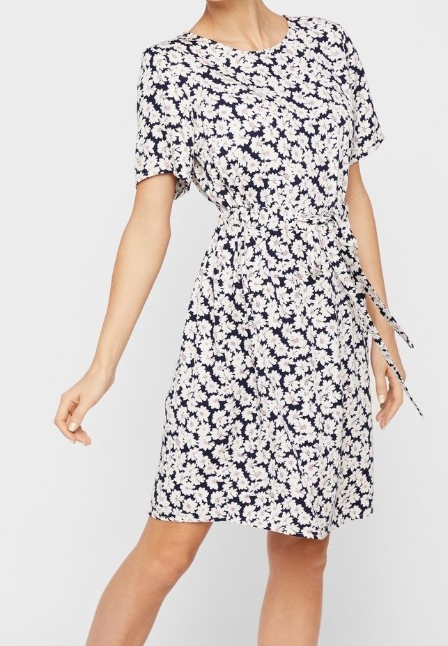 Woman wearing a knee-length, short-sleeve navy dress with white floral print and a fabric belt tied at the waist.