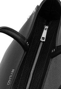 Black textured leather handbag with silver zipper and dual handles, showing interior opening and partial brand logo "RYLKO" on outer side.