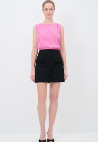 Mouwloze roze blouse gecombineerd met een zwart hoge taille rok met voorknopen en zijzakken. Glad textuur door het geheel.