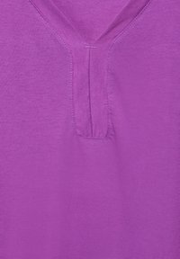 Haut en coton violet à col en V avec un détail de patte de boutonnage cousue, texture lisse, manches courtes et couleur unie sans motifs ni embellissements.