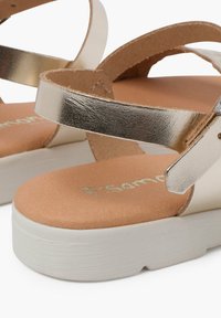 Sandalias de plataforma blancas con correas metálicas plateadas. Textura suave del plantillado en tono bronceado con el nombre de la marca en relieve y detalle de hebilla ajustable.