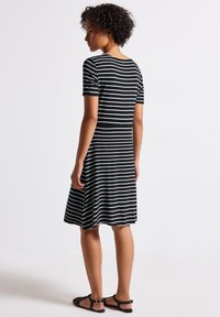 Schwarz-weiß gestreiftes Kleid mit kurzen Ärmeln, tailliertem Oberteil, ausgestelltem Rock und strukturiertem Stoff. Getragen mit flachen schwarzen Sandalen.