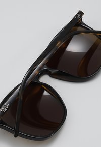 Ochelari de soare Ray-Ban cu rame negre și cu model de țestoasă, lentile maro și brațe subțiri cu un logo. Finisaj din plastic neted.