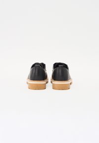 Black leather shoes with a smooth finish, rubber soles, tan accents, and stitched detailing at the base, viewed from the back.