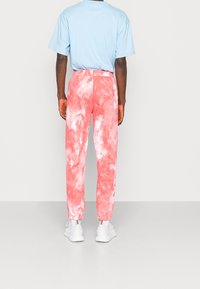 Unisex blå t-shirt och rosa tie-dye byxor med elastiska muddar, tillsammans med vita träningsskor.