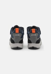 Zapatillas mid-top en navy y gris con una superficie texturizada, que cuentan con una pestaña en el talón de color naranja y correas de Velcro para un ajuste seguro. Marca Geox visible.