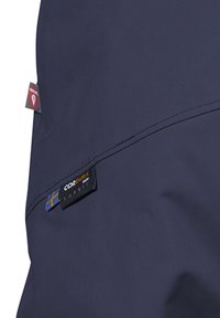 Marinblå tygjacka med en slät yta, förstärkta sömmar och flera etiketter, inklusive en Cordura-etikett och tillverkarens märke.