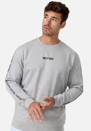 Sweatshirt gris en coton, avec des manches longues. Logo noir "INDICODE" au niveau de la poitrine et sur les coutures latérales. Poignets et ourlet côtelés.
