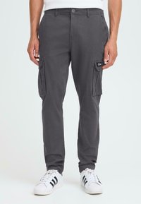 Grå cargo-bukser med to sidelommer, laget av et holdbart stoff. Har knappelukking og belteklips, parret med hvite sneakers.