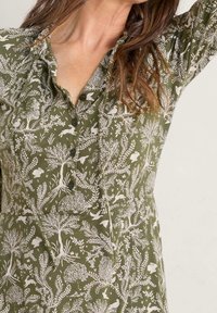 Groene jurk met een botanisch ontwerp, voorzien van witte bomen en dieren, knoopsluitingen en een zachte textuur.