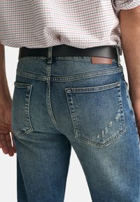 Ljusblå denimjeans med en urtvättad finish, fem fickor och en brun läderetikett på baksidan av midjebanden. Tyget visar lätt slitage.