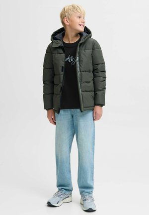 Zelena puffer jakna s kapuljačom, s horizontalnom quilted teksturom, prednjim zatvaračem i tamnim akcentima. Nosi se preko crne majice i svijetlih traperica.
