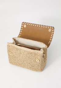 Liten rektangulær beige vevd håndveske med åpen tan skinnklaff og innvendig glidelåslomme, vist mot hvit bakgrunn.