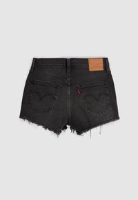 Short en denim noir avec ourlets effilochés, deux poches arrière avec détails de couture, écusson en cuir de la marque et petite étiquette rouge sur la poche droite.