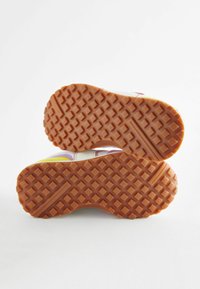 Semelle en caoutchouc orange avec une surface texturée et à motifs, dotée d'un relief prononcé pour une meilleure adhérence. Design supérieur multicolore vif visible sur les bords.
