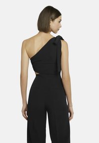 Zwart één-schoudertop met een gestrikt accent, met een getailleerde pasvorm en een open rugontwerp, gecombineerd met wijde broekspijpen.