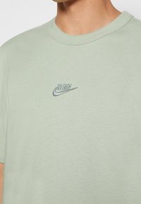 Camiseta verde claro fabricada en algodón, con una textura suave, cuello redondo y un logotipo de Nike bordado en color contrastante.