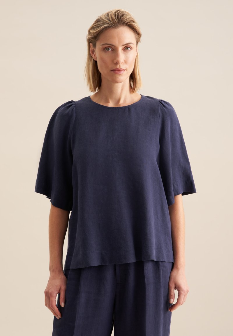 Top in lino blu navy con maniche corte a sbuffo, scollatura rotonda e vestibilità ampia, caratterizzato da un orlo diritto e una texture minima.