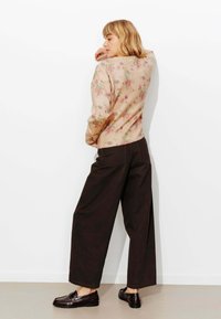 Pull floral rose clair avec poignets côtelés, associé à un pantalon large marron foncé et des chaussures noires brillantes, présenté sur un fond blanc.