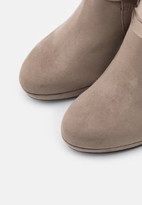 Botas de tobillo de ante beige con puntera redondeada, textura suave y diseño minimalista, que presentan una costura discreta a lo largo de la suela.