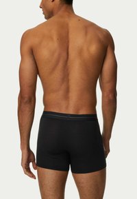 Svarta boxerkalsonger i mjukt tyg, med svart elastiskt midjeband med en subtil logotyp, åtsittande design och längd till mitten av låret.