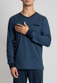 Marineblauwe langermige V-hals shirt met een gestructureerde stof en een klein borstzakje, gecombineerd met gestreepte marineblauwe broek; heeft contrasterende mouwen.