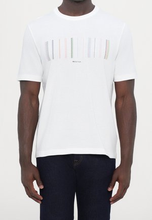Homme portant un t-shirt blanc à manches courtes avec des lignes verticales pointillées multicolores et un petit texte « PS Paul Smith » sur la poitrine.