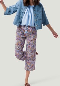 Veste en jean, blouse bleu clair et pantalon court à motifs avec un design cachemire multicolore et taille à cordon. Sandales plates marron.