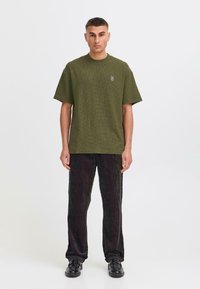 Olive green short-sleeve textured shirt with a round neckline, paired with black ribbed pants, worn with black shoes. Simple design, casual fit.