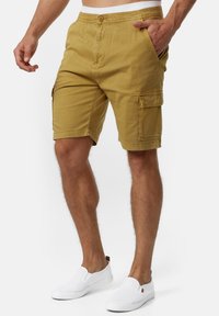 Bomulds cargo shorts i khaki, midt på låret med knaplukning, sidelommer og en stor cargo lomme. Båret med hvide slip-on sko.