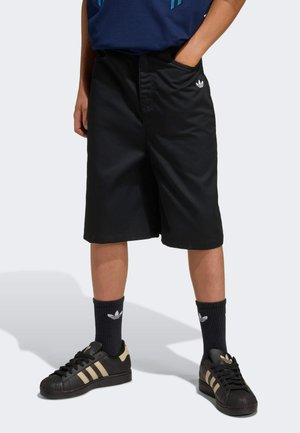 Black shorts made of lightweight fabric with a relaxed fit, featuring side pockets and a small white logo on the left. Paired with black sneakers.