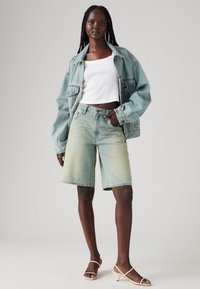 Svetlo modra jeans jakna z ohlapnim krojem, bel ovratni top v obliki kratkega zgornjega dela in svetlo zelene jeans kratke hlače. Dodatki vključujejo bež sandale z visokimi petami.