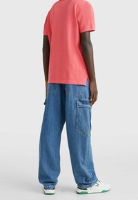 Korallfärgad bomulls-T-shirt kombinerad med lösa blå denim cargo-byxor med flera fickor, avslutad med vita skor med gröna accenter.