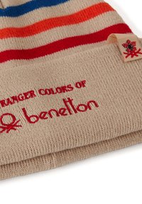 Pletená čepice v béžové barvě s vodorovnými pruhy v modré, oranžové a červené. Vyšitý nápis "stranger colors of benetton" červeně. Štítek s logem.