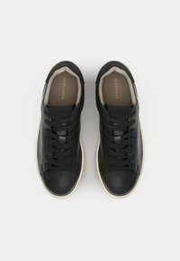 Sneaker in pelle nera con profilo basso, punta tonda, lacci piatti e suole in gomma di colore chiaro. L'interno è foderato in beige e presenta il branding.