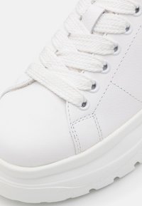Vita sneakers med en texturerad yta, runda vita snörning, förstärkt sömnad och en tjock vit gummisula. Minimalistiska designdetaljer.