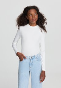 Top bianco a maniche lunghe con scollo rotondo, abbinato a jeans in denim azzurro chiaro a vita alta. Texture liscia e silhouette aderente.