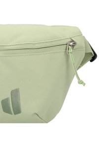 Lichtgroene stoffen heuptas met een ritssluiting, voorzien van een kleine trekkoord en een donkergroen logo dat aan de zijkant is gedrukt.