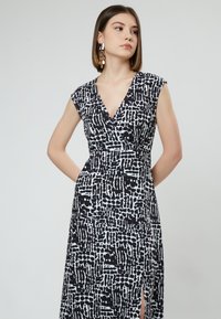 Vestido negro y blanco con estampado, con escote en V, mangas cortas y una abertura lateral. La tela parece suave con un diseño de corte holgado.
