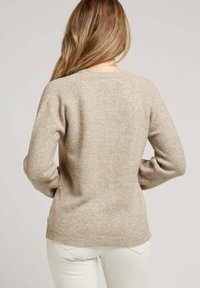 Pull légère beige en tricot doux, avec un col rond, des manches longues, et des bords côtelés aux poignets et à l'ourlet.