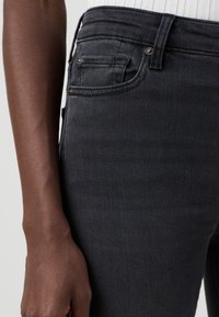 Jeans in denim nero con un design aderente, caratterizzati da dettagli di cucitura sottili, una tasca frontale visibile e una superficie liscia e strutturata.
