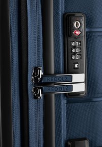 Valise bleue texturée avec cadenas à combinaison TSA noir et deux curseurs de fermeture éclair bleu foncé étiquetés "REDOLZ", sécurisés sur la glissière.