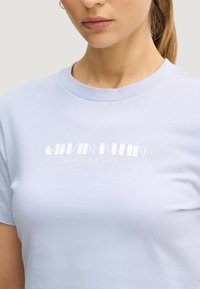 Jasnoniebieska bawełniana koszulka z okrągłym dekoltem i białym nadrukiem logo "CALVIN KLEIN NEW YORK CITY" na piersi.
