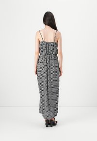Robe longue à motifs noir et blanc avec bretelles spaghetti, taille froncée et silhouette fluide. Le tissu semble léger, texture lisse.