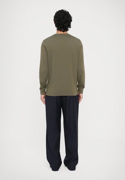 Μπλούζα με μακριά μανίκια σε λαδί πράσινο χρώμα με στρογγυλή λαιμόκοψη, συνδυασμένη με φαρδιά παντελόνια σε σκούρο μπλε με λεπτές ρίγες. Μαλακό ύφασμα, άνετη εφαρμογή.