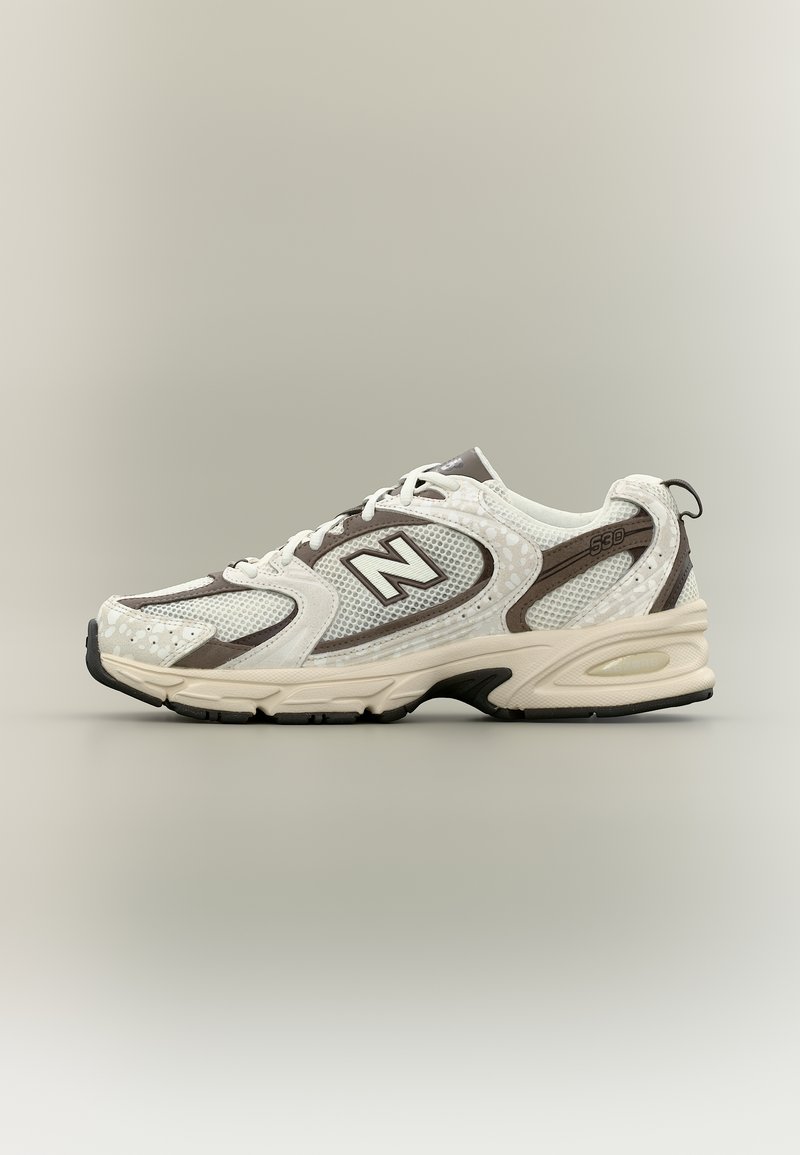 Pantof sport New Balance 530 alb și gri, cu partea superioară din plasă, design cu șireturi și talpă amortizată pe un fundal neutru.