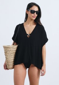 Črna lahka obleka s kratkimi rokavi in globokim V-izrezom, prilagojena za čez kopalke. Doplačana z tkanim slamnato torbo.