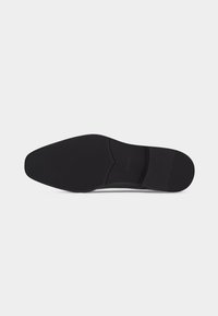 Semelle de chaussure de ville noire avec une texture lisse et élégante, talon et zones d'orteils définis, présentée sur un fond gris clair uni.